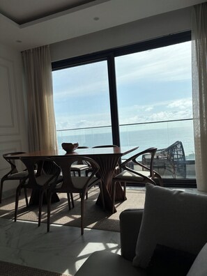 Ein modernes Zimmer mit Esstisch und Stühlen, einer Couch und einem großen Fenster mit Meerblick.