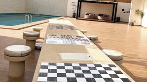 Área de piscina com piso xadrez, espreguiçadeiras e um espaço de estar com lareira.