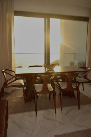 Un espace repas comprenant une table et des chaises, une vue sur la mer grâce à de grandes fenêtres et un aménagement intérieur moderne.
