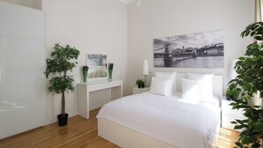 A bedroom with a bed, a desk, a chair, a potted plant, a mirror, and a wall-mounted picture. - Flatiron Budapest by Hi5 (Budapest)