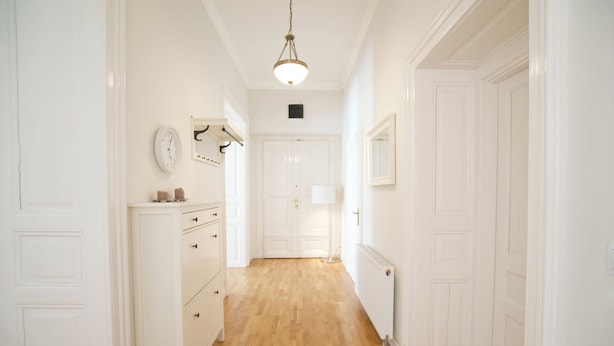 A hallway with white walls, a wooden floor, a clock, a radiator, and a door at the end. - Flatiron Budapest by Hi5 (Budapest)