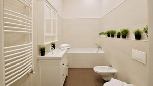 A modern bathroom with a bathtub, sink, and toilet. There are potted plants on a shelf above the sink. - Flatiron Budapest by Hi5 (Budapest)