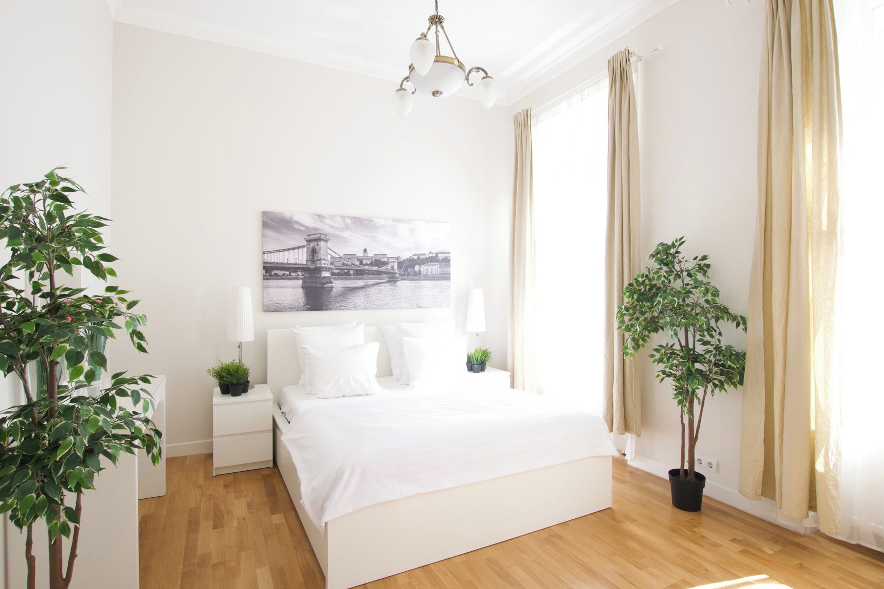 Une chambre à coucher avec un lit, des tables de chevet, une lampe, un tableau accroché au mur et deux plantes en pot.