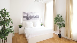 A bedroom with a bed, bedside tables, a lamp, a wall-mounted picture, and two potted plants. - Flatiron Budapest by Hi5 (Budapest)
