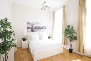 A bedroom with a bed, bedside tables, a lamp, a wall-mounted picture, and two potted plants. - Flatiron Budapest by Hi5 (Budapest)