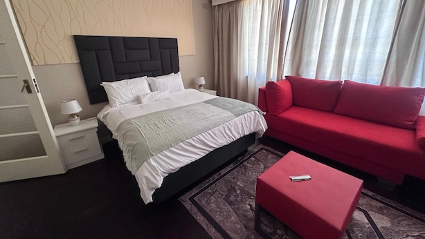Hotellihuone, jossa on sänky, punainen sohva, pieni pöytä ja yöpöytä, jossa on lamppu.