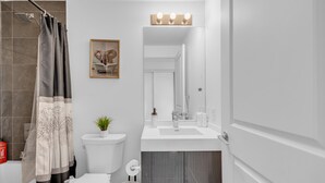 Uma casa de banho moderna com chuveiro, sanita e lavatório, e um espelho sobre o lavatório.