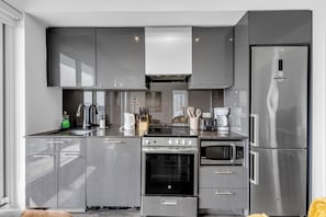 Eine moderne Küche mit grauen Schränken, einem Edelstahlkühlschrank, einem eingebauten Backofen, einer Mikrowelle und einem Gasherd.