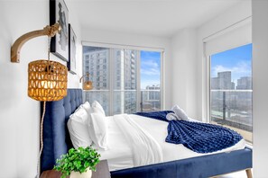 Ein modernes Schlafzimmer mit großem Fenster, blauer Bettdecke und einer dekorativen Wandleuchte.