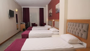 Une chambre d’hôtel avec trois lits, une télévision, une petite table et un miroir.