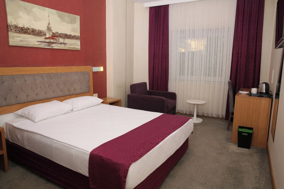 Une chambre d’hôtel avec un lit, une chaise, une petite table, un bureau et un tableau au mur.