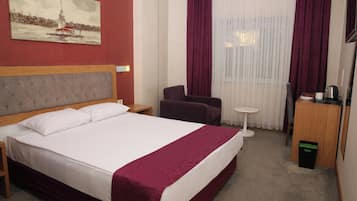 A hotel room with a bed, a chair, a small table, a desk, and a painting on the wall.