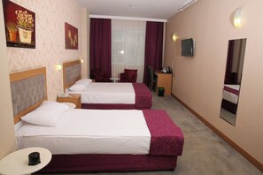 Ein Hotelzimmer mit zwei Betten, einem Schreibtisch, einem Stuhl, einem kleinen Tisch und einem Spiegel.