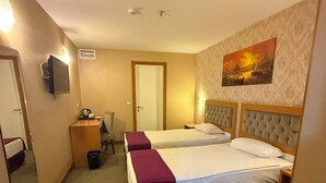 Une chambre d’hôtel avec deux lits, un bureau, une chaise, une télévision et un tableau au mur.