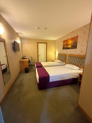 Ein Hotelzimmer mit zwei Betten, einem Schreibtisch, einem Sessel, einem Fernseher und einem Gemälde an der Wand.