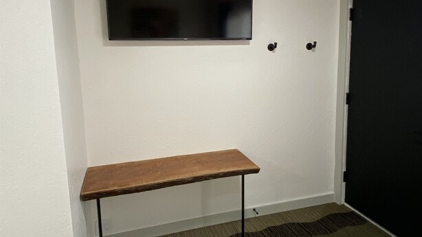Ein Hotelzimmer mit einem wandmontierten Flachbildfernseher, einer hölzernen Bank und einer Tür.