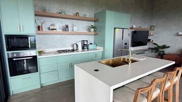 Une cuisine moderne avec des meubles de couleur turquoise, un îlot central doté de tabourets de bar et un micro-ondes encastré.