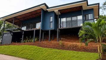 A modern two-story house with a flat roof, large windows, and a covered porch area.