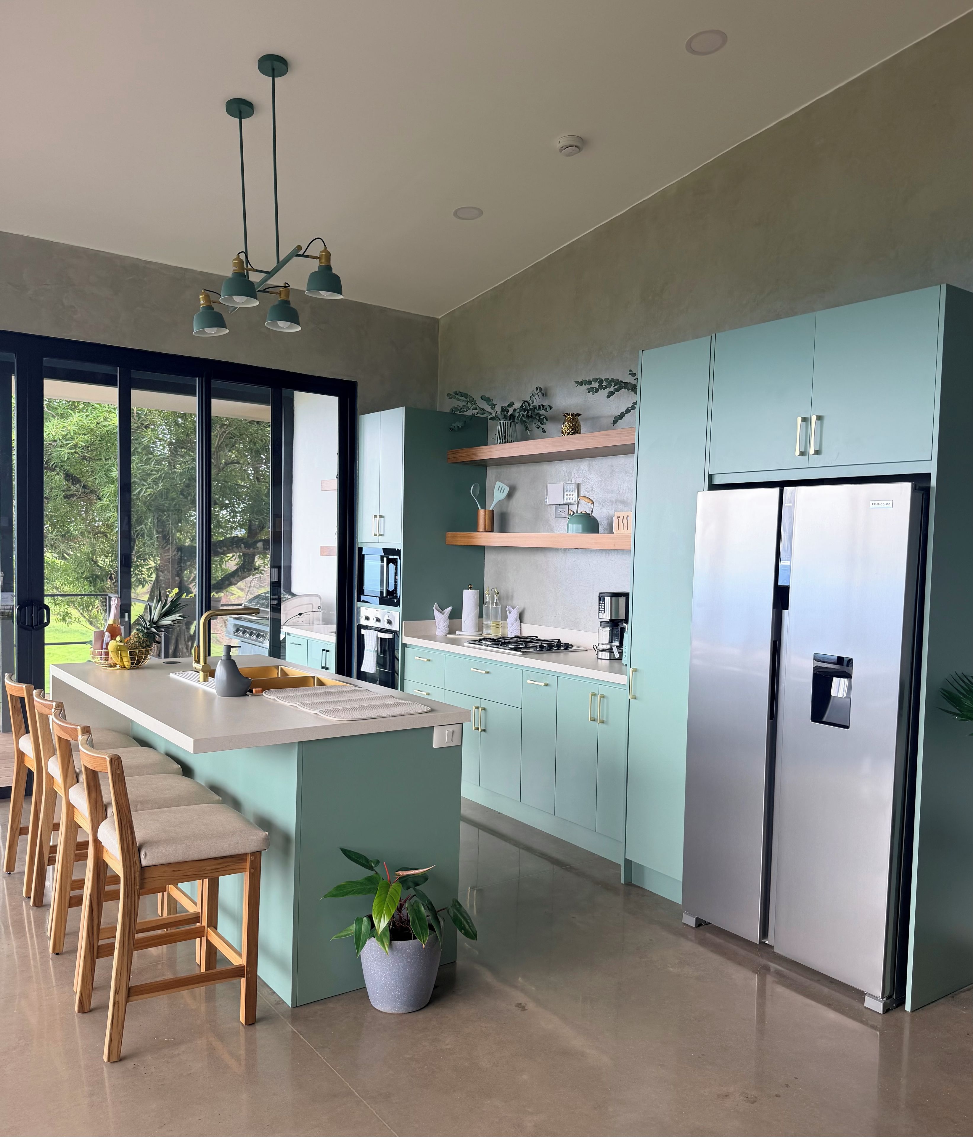 A modern kitchen with a central island, stainless steel appliances, and a view of greenery outside.