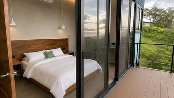 A bedroom with a bed, a nightstand, and a window with a view of greenery.