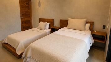 A hotel room with two beds, wooden headboards, bedside tables, and an air conditioning unit.