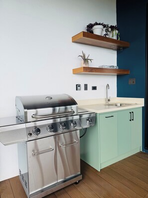 A kitchen with a stainless steel stove, a sink, light green cabinets, and a wooden shelf with plants. - Aurelia | Exclusive Mountain Villa near Monteverde (Abangares)