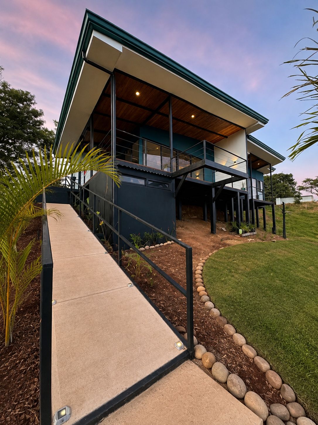 A modern house with a covered porch, a concrete pathway, and a landscaped garden.