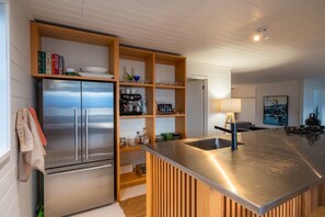 A modern kitchen with a stainless steel refrigerator, wooden shelves, and a central island with a sink.
