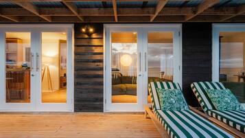A wooden deck with a glass door entrance leading to a room with a bed and a lamp.