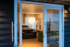 A room with a bed, a chair, a small table, and a large window.