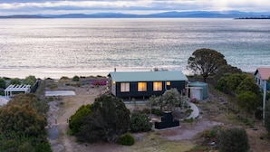 A coastal property with a house overlooking a large body of water, surrounded by vegetation and a clear sky.