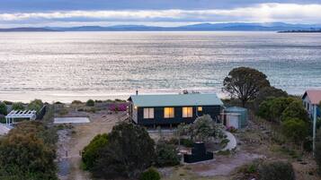 A coastal property with a house overlooking a large body of water, surrounded by vegetation and a clear sky.