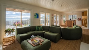 A modern living room with a green sectional sofa, a coffee table, and a view of the sea through large windows.