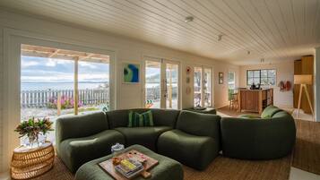 A modern living room with a green sectional sofa, a coffee table, and a view of the sea through large windows.