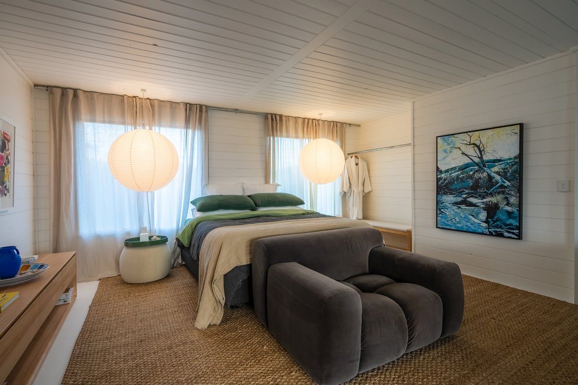 A bedroom with a bed, bedside table, lamp, and artwork.