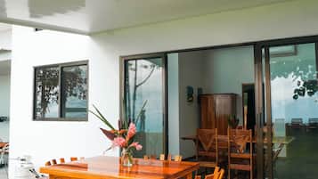 Un'area pranzo esterna moderna con tavolo e sedie in legno, un vaso di fiori e vista sull'interno tramite porte in vetro.