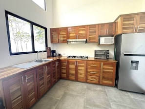 Una cucina moderna con mobili in legno, un frigorifero in acciaio inossidabile, un forno a microonde, un fornello a gas e una finestra che lascia entrare luce naturale.