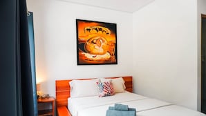 Quarto de hotel com cama, almofadas, um quadro pendurado na parede e uma mesa de cabeceira com abajur.