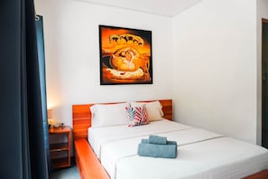Una camera d'albergo con un letto, cuscini, un quadro appeso al muro e un comodino con una lampada.