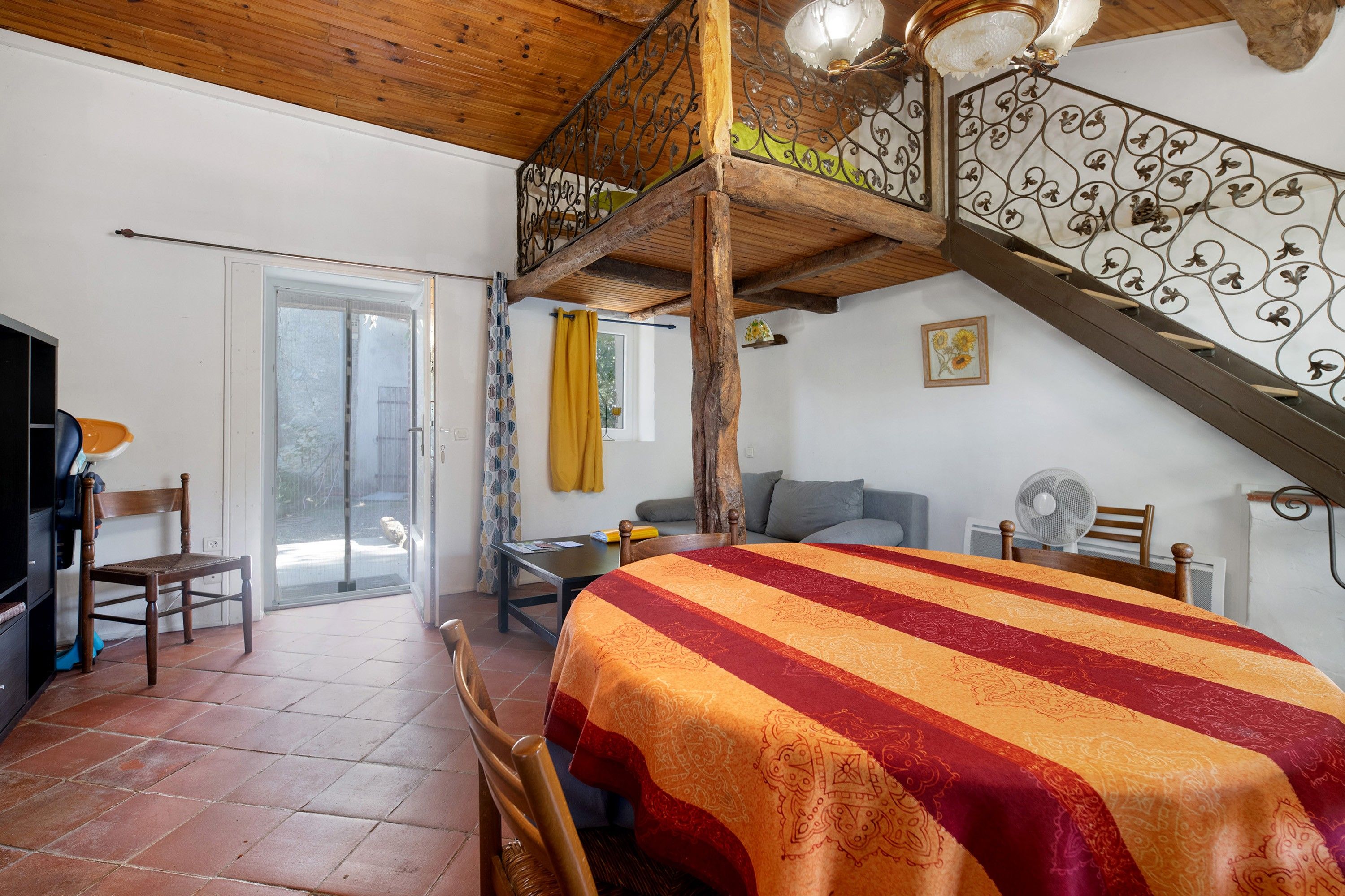 A room with a bed, a table, a chair, a staircase, and a view of the outside.