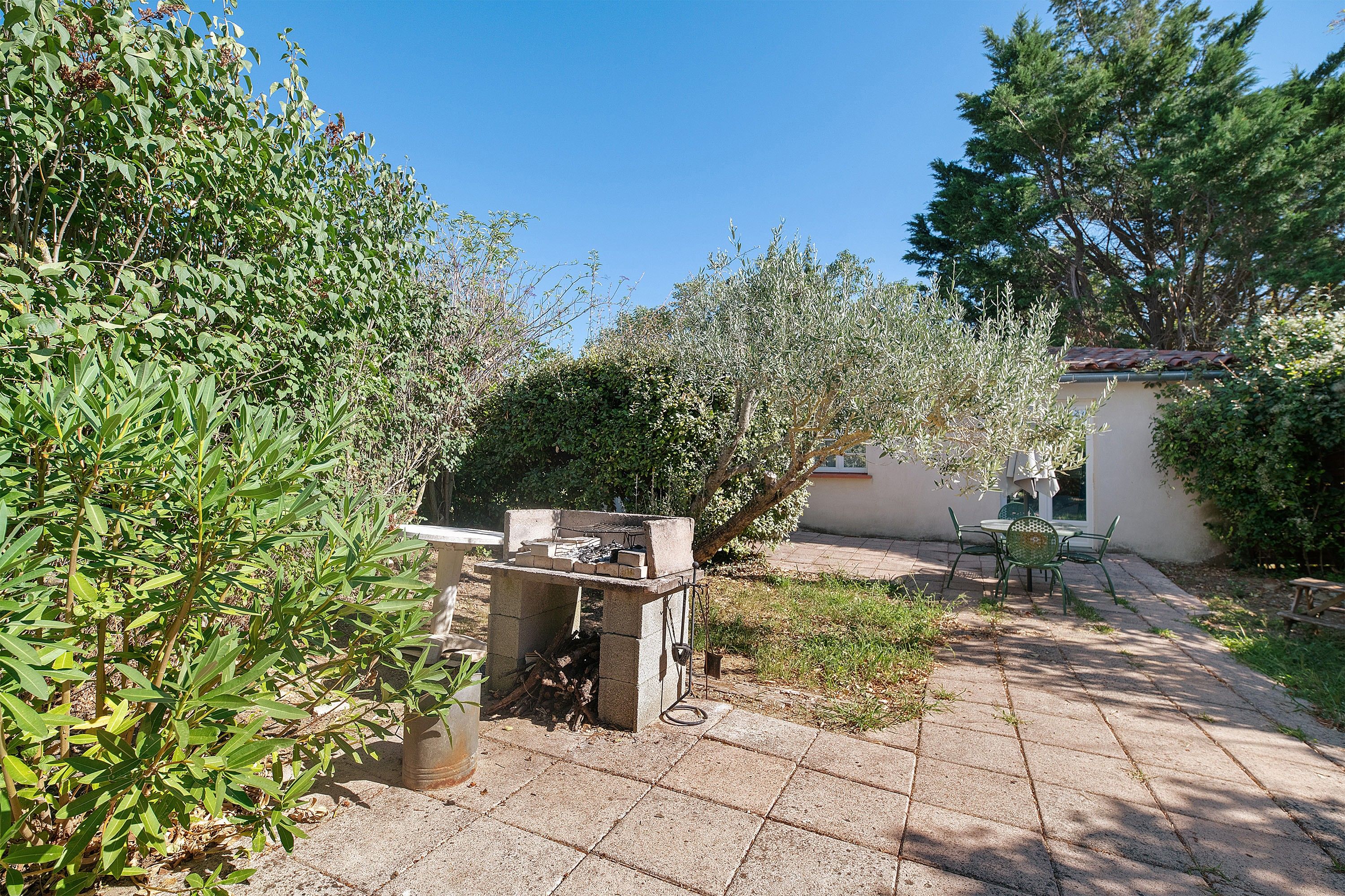Un espace patio aménagé avec un barbecue, des sièges d’extérieur et une variété de plantes.