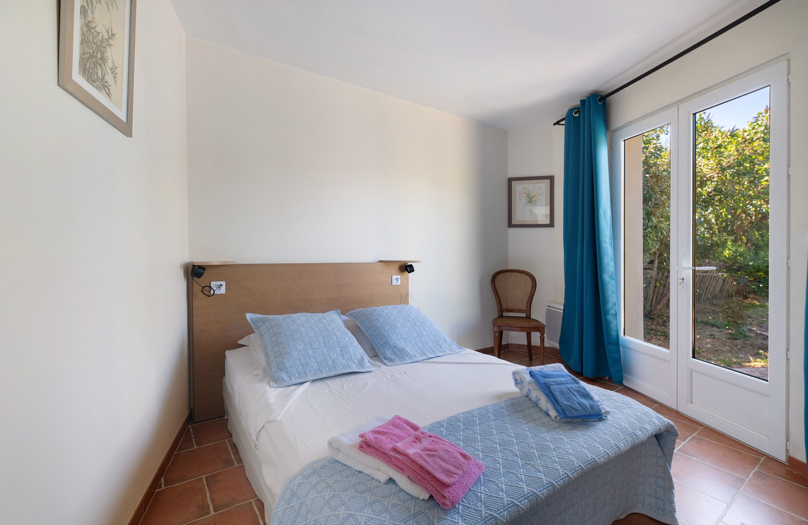 Une chambre à coucher avec un lit, des oreillers, une chaise et une fenêtre avec des rideaux.