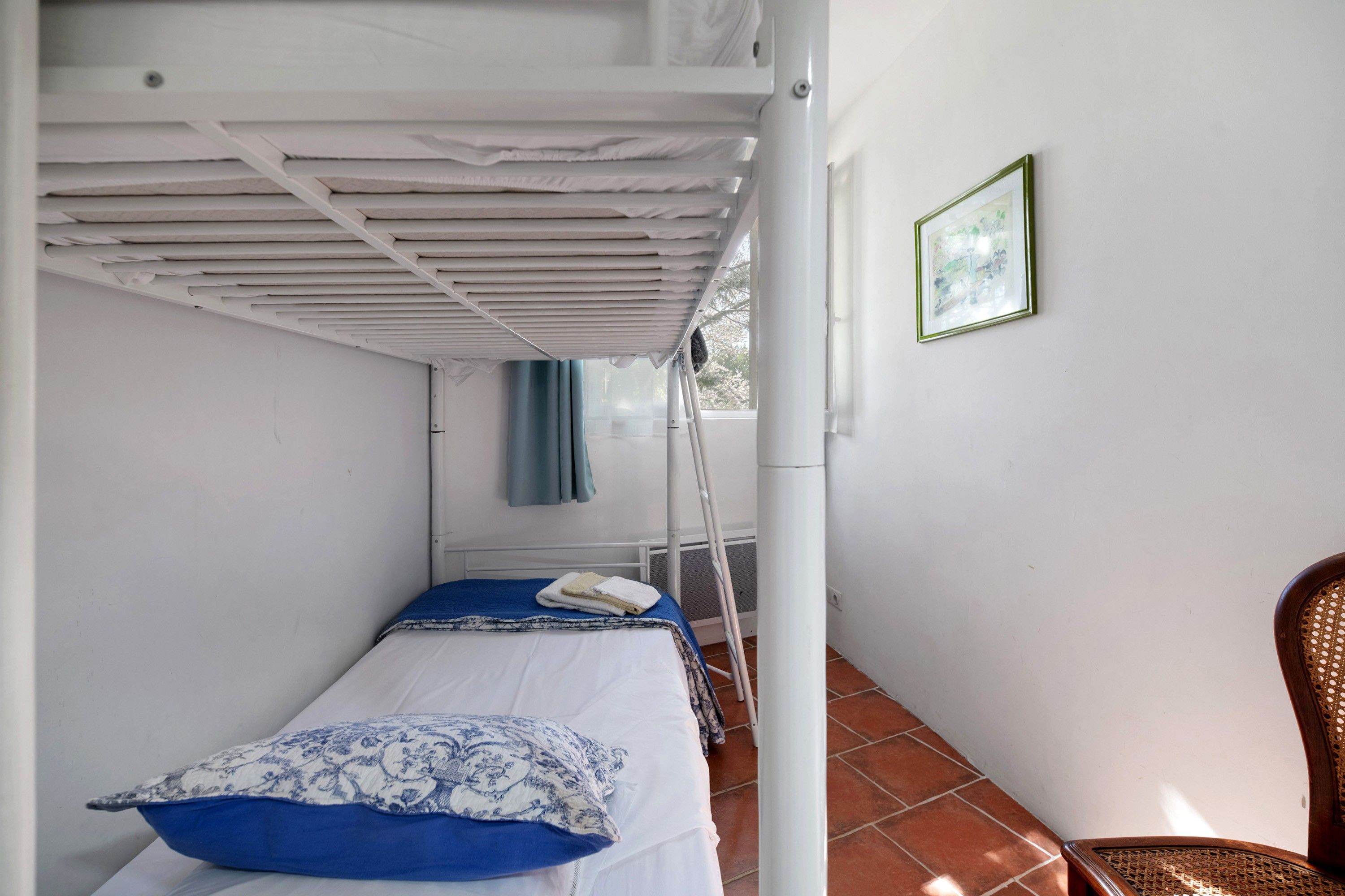 A narrow room with a bunk bed, a chair, and a framed picture on the wall.