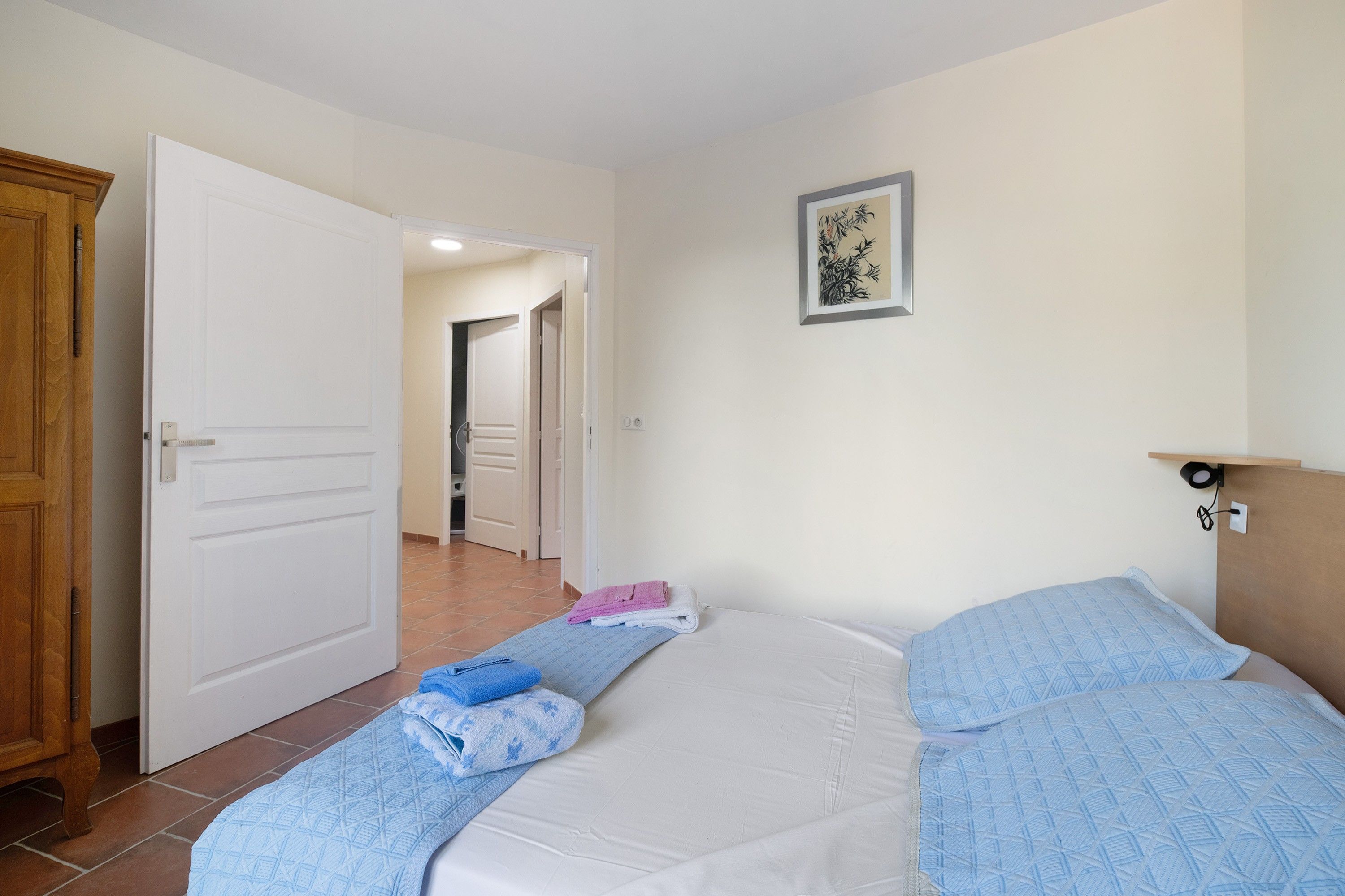 A hotel room with a bed, a wooden wardrobe, a bathroom visible through an open door, and a framed picture on the wall.