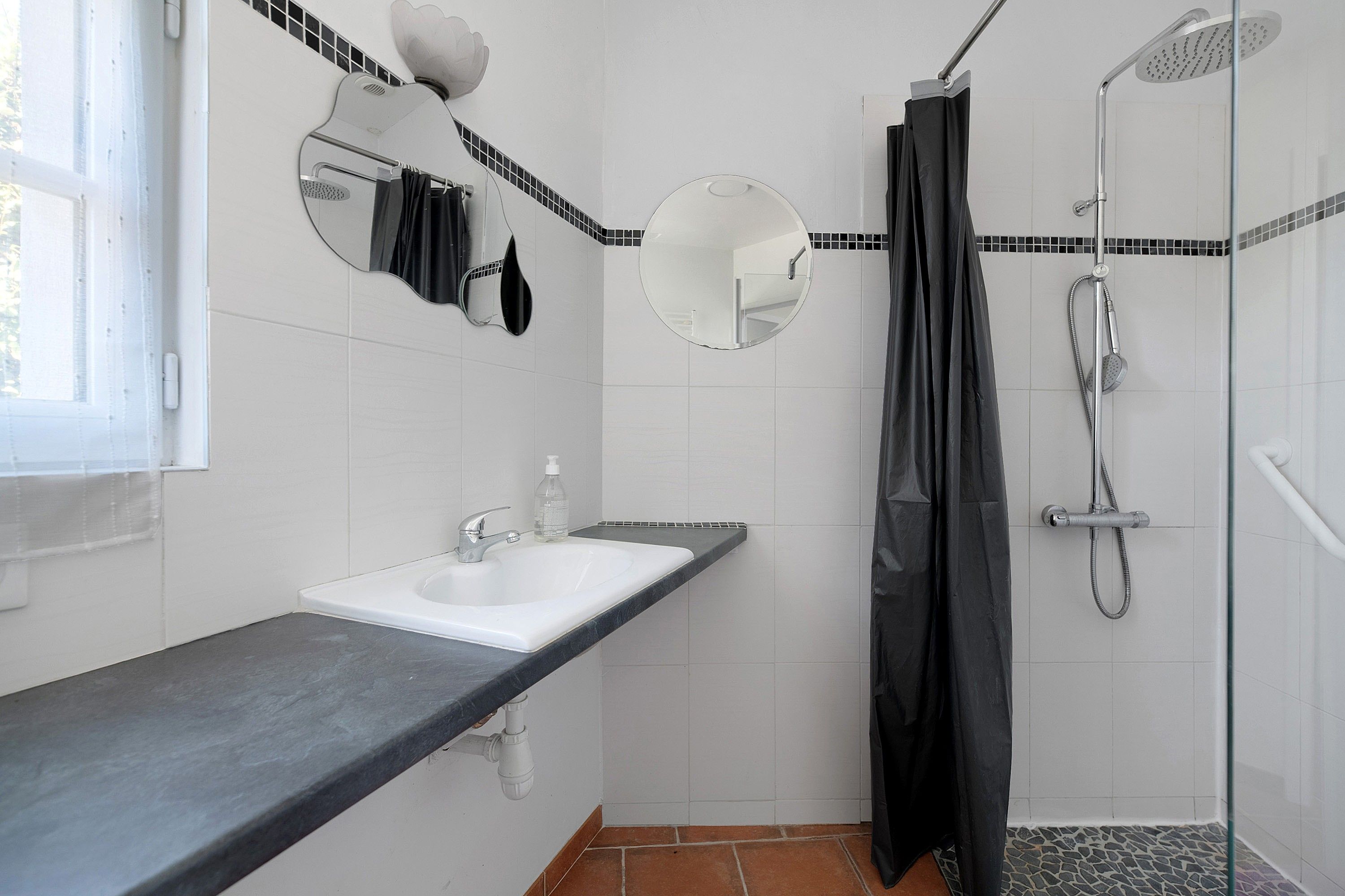 Un baño con lavamanos blanco, un espejo, ducha y cortina de ducha negra.