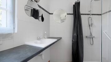 Un baño con lavamanos blanco, un espejo, ducha y cortina de ducha negra.