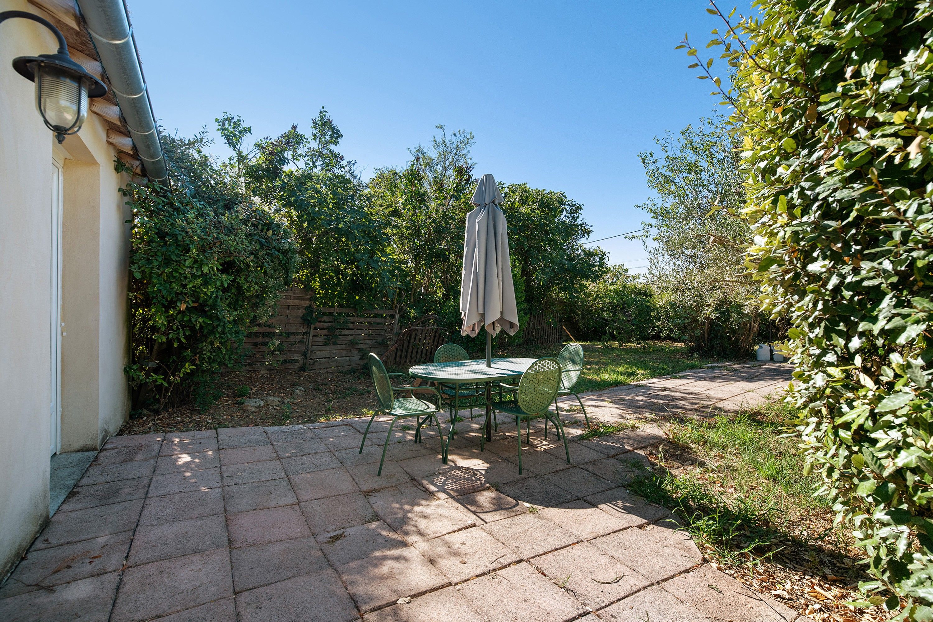 A patio with a table and chairs, surrounded by greenery and a stone wall.