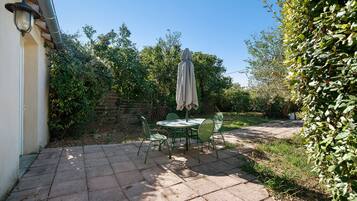 Une terrasse avec une table et des chaises, entourée de verdure et d’un mur en pierre.