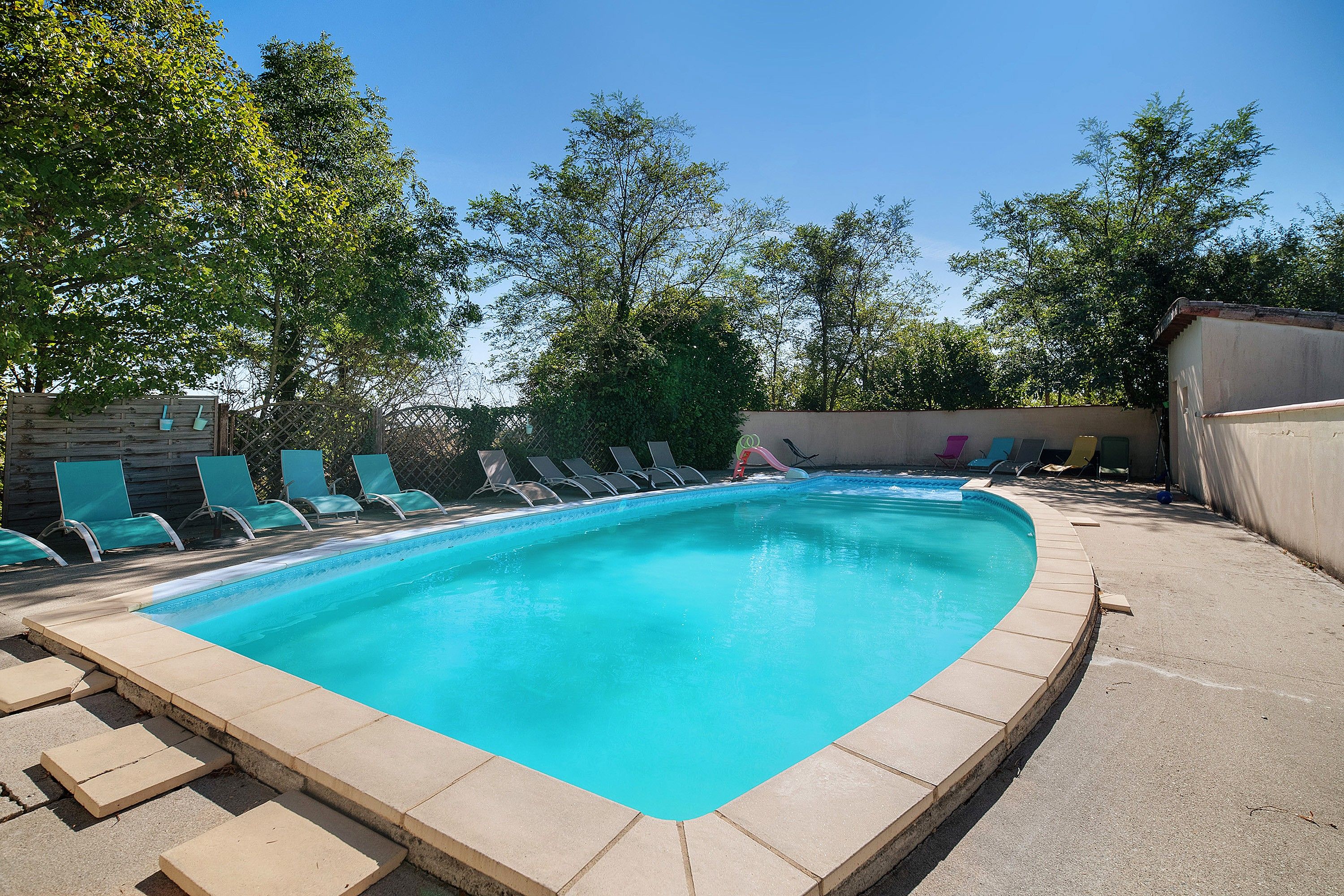 Une piscine rectangulaire dont le bord est recouvert de carrelage, entourée d’une terrasse en béton.
