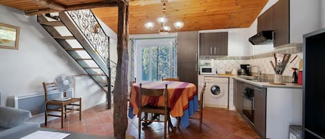 A rustic kitchen with a dining area, wooden ceiling, and a staircase.